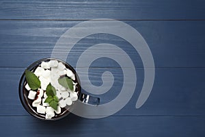 Glass cup of delicious hot chocolate with marshmallows and fresh mint on blue wooden table, top view. Space for text
