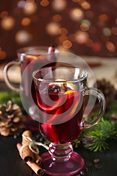 Glass cup of delicious mulled wine on wooden table against blurred lights
