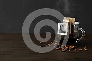 Glass cup with drip coffee bag and beans on black wooden table. Space for text