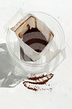 Glass cup with drip coffee bag on white background with copy space. Opened Instant paper sachet.