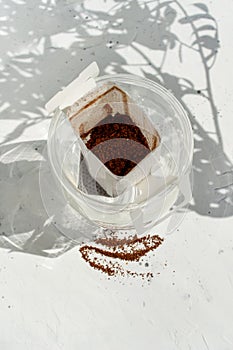 Glass cup with drip coffee bag on white background with shadow and copy space. Opened Instant paper sachet.