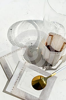 Glass cup with drip coffee bags on white background with copy space. Opened Instant espresso home brew bags still life