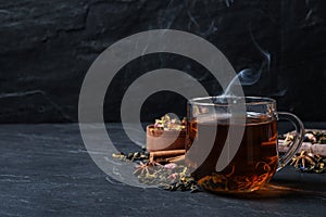 Glass cup of freshly brewed tea and dry leaves on black table. Space for text
