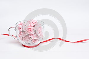 Glass cup full of pink roses with red ribbon around it on white