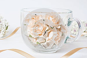 Glass cup full of white roses with ribbon on wooden table