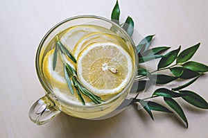 Glass cup of ginger tea with lemon, rosemary served round frame green leaves ruscus flowers on a light wooden rustic