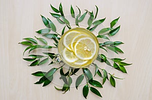 Glass cup of ginger tea with lemon served round frame green leaves ruscus flowers on a light wooden rustic wall