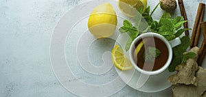 Glass cup of ginger tea with lemons and mint leaves on light background. Ginger tea, drink, cold and autumn time. Banner