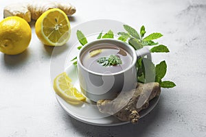 Glass cup of ginger tea with lemons and mint leaves on light background. Ginger tea, drink ingredients, cold and autumn time