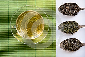 Glass cup of green tea on geen napkins and three spoons with varios kind of tea.