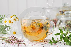 Glass cup of healthy calendula herbal tea, healing heather, chamomile and salvia medicinal herbs and flowers on table.