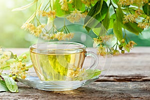 Glass cup of healthy tea with linden tree flowers on wooden board, lime tree flowers.