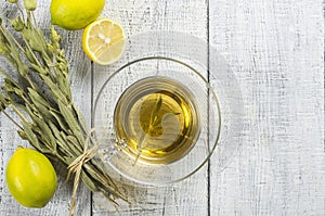 Glass cup of herbal sage tea with dried sage leaves and lemon on white wooden rustic background