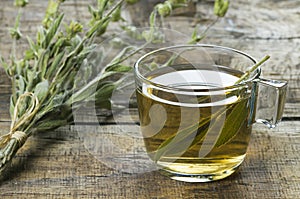 Glass cup of herbal sage tea with dried sage leaves on wooden rustic background