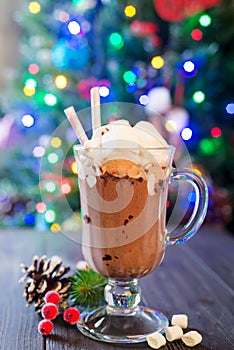 Glass cup of hot cocoa with mini marshmallows with pine boughs a rustic background with beautiful Christmas lights of