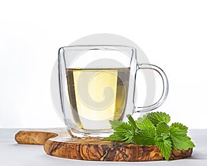 Glass cup of hot green tea with mint on wooden stand on white background