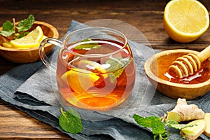 A glass cup of hot tea with lemon, mint, ginger and honey on wooden rustic table