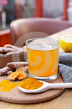 Glass cup of hot tea, lemon, turmeric powder and roots on wooden table