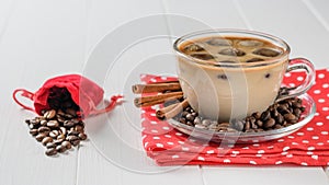 Glass Cup with ice coffee and coffee beans spilling out of the bag on a white table