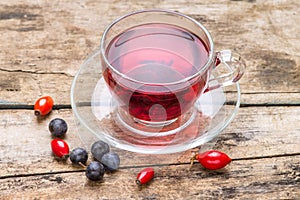 Glass Cup of karkade tea with wild berries on wood background