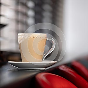 Glass cup of latte or cappuccino coffee with froth on blurred background. Aromatic hot drink on windowsill in cafe. Copy