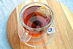 Glass cup, mug of red colored, hot Rooibos or red bush tea, on a wooden plate, aromatic drink, beverage, tonic, stimulant