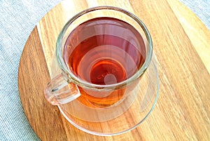 Glass cup, mug of red colored, hot Rooibos tea or red bush tea on a wooden plate, aromatic drink, beverage, tonic, stimulant