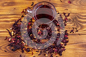 Glass cup of red hibiscus tea carcade, roselle on wooden table