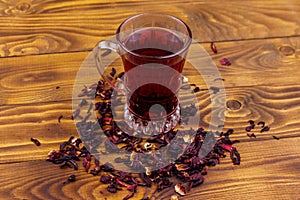 Glass cup of red hibiscus tea carcade, roselle on wooden table