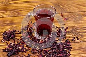 Glass cup of red hibiscus tea carcade, roselle on wooden table