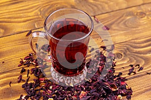 Glass cup of red hibiscus tea carcade, roselle on wooden table