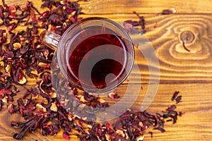 Glass cup of red hibiscus tea carcade, roselle on wooden table