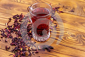 Glass cup of red hibiscus tea carcade, roselle on wooden table