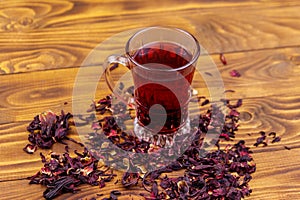 Glass cup of red hibiscus tea carcade, roselle on wooden table