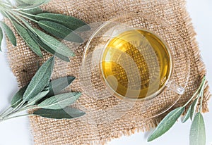 Glass cup with sage tea and sage leaves on jute and white wood