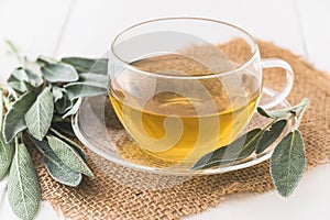 Glass cup with sage tea and sage leaves on jute and white wood