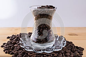Glass cup on saucer with coffee beans on wooden table