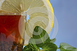 Glass cup of strong black tea on a beautiful blue background with a yellow lemon and green mint.