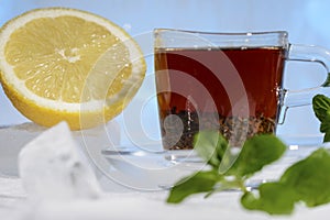 Glass cup of strong black tea on a beautiful blue ice with yellow lemon and green mint.