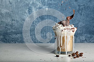 Glass cup of tasty coffee with whipped cream and chocolate on table against color background.