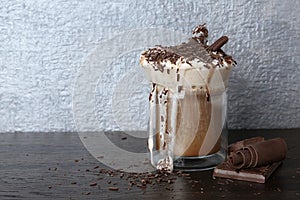 Glass cup of tasty coffee with whipped cream and chocolate on wooden table.
