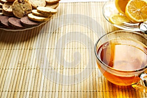 Glass cup of tea with biscuits and lemon on a light wooden background.Cup of tea with lemon and biscuits