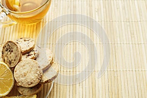 Glass cup of tea with biscuits and lemon on a light wooden background.Cup of tea with lemon and biscuits