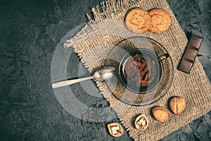 Glass cup of tea with cookies, walnuts and chocolate on a burlap napkin on a dark concrete background. stylized creative mockup