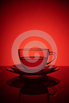 Glass cup of tea on a glass saucer with reflection, with a gradient of black and red background. Concept, healthy and