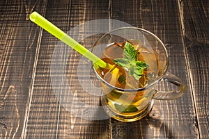 In a glass cup tea with lemon and ice, mint and straw, cold tea