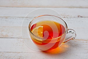 Glass cup with tea and lemon standing on a white painted wooden surface. Background for hot drinks. Soft and tonic drinks