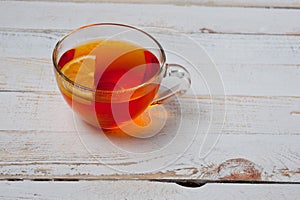 Glass cup with tea and lemon standing on a white painted wooden surface. Background for hot drinks. Soft and tonic drinks