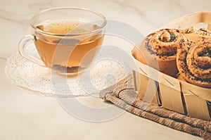 glass cup of tea and rolls with poppy /glass cup of tea and rolls with poppy in a wooden basket on a white table