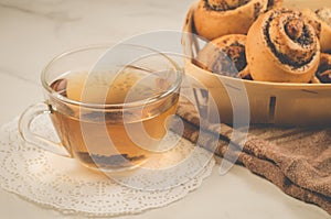 glass cup of tea and rolls with poppy in a wooden basket/glass cup of tea and rolls with poppy in a wooden basket on a white table